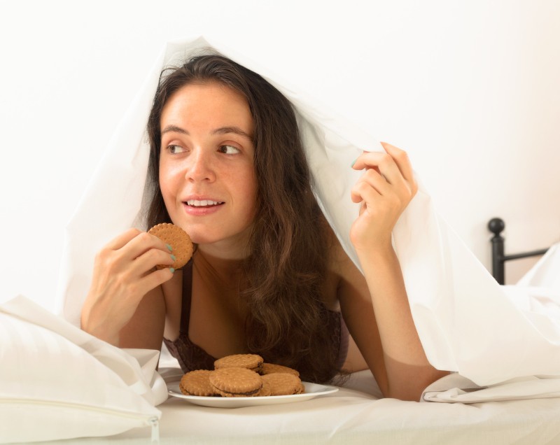 Девушка ест печенье в постели и раздевается